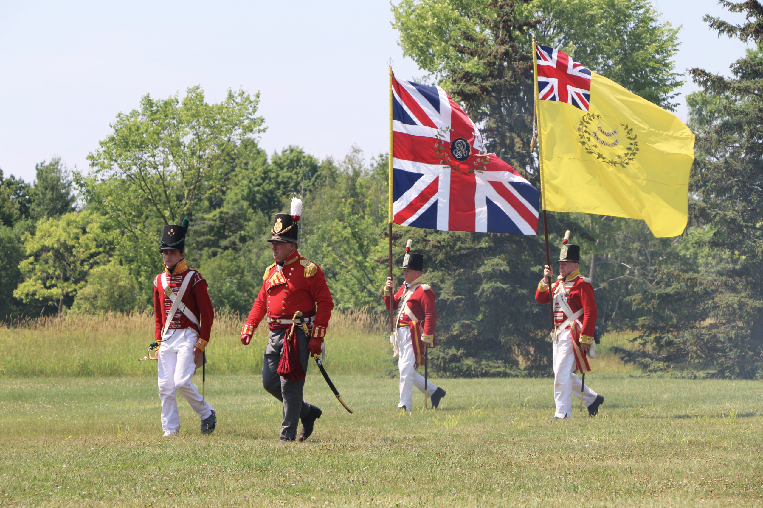 Soldiers wearing red military uniforms marching with flags in hand.
